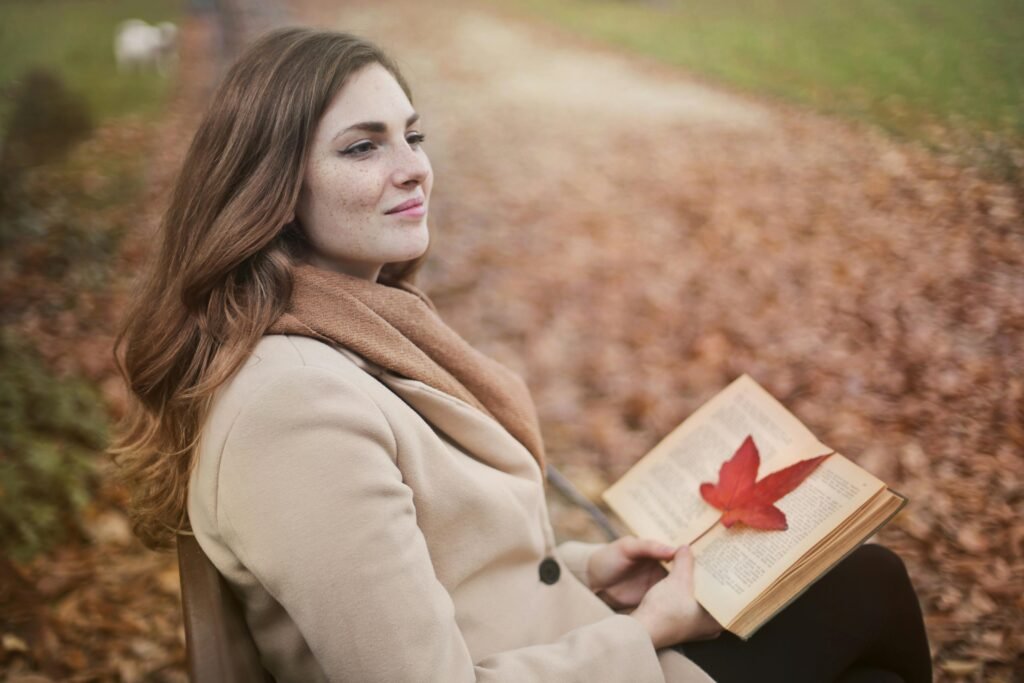 pexels-photo-3769732-3769732 Side view of peaceful young female in warm coat and scarf sitting on bench with open book in hands and looking away pensively while resting in autumn park